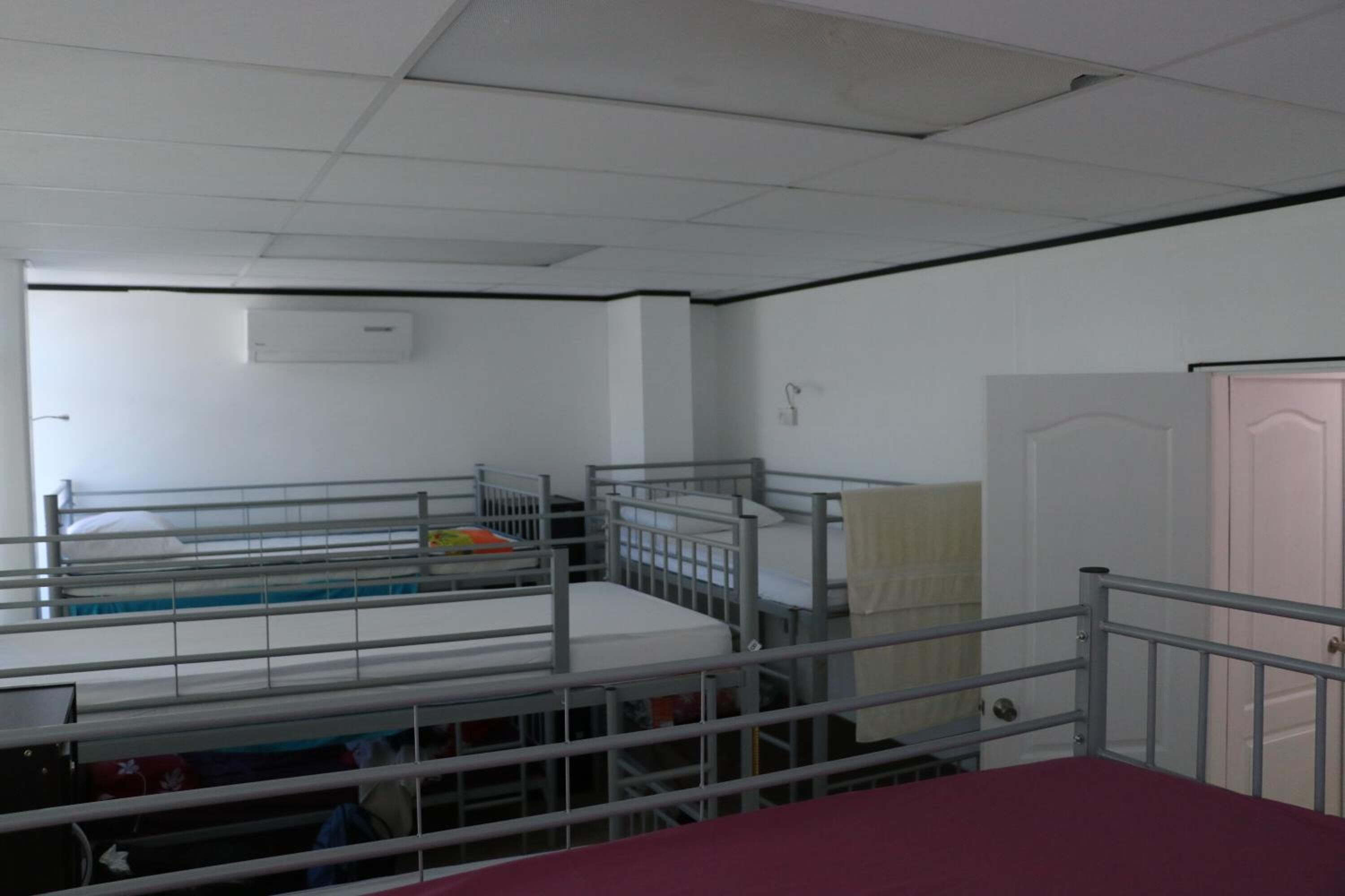 Une chambre de dortoir avec des lits superposés, un climatiseur blanc, une porte et une fenêtre.
