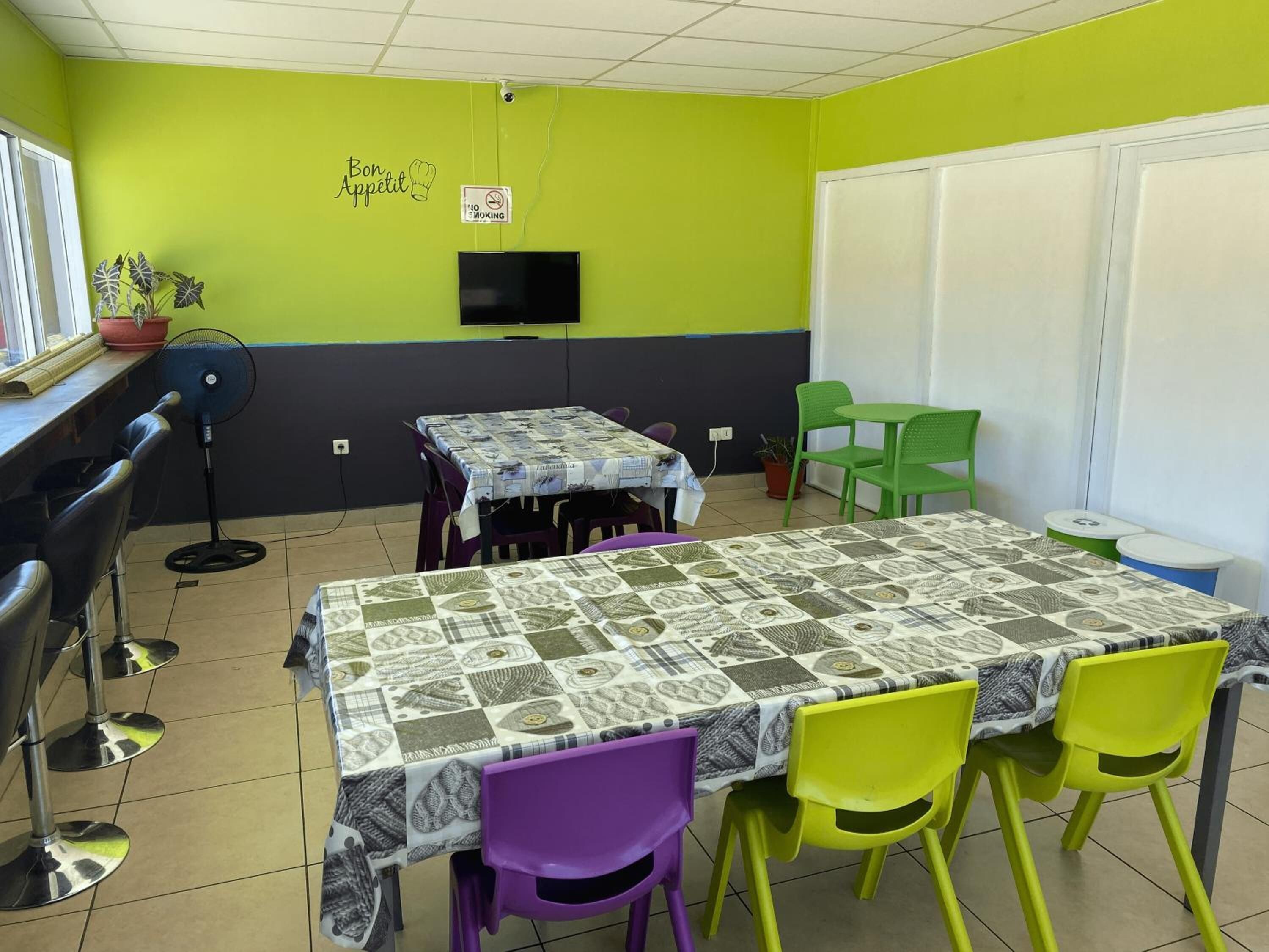 Un comedor con una mesa cubierta por un mantel estampado, rodeado de sillas moradas y verdes.