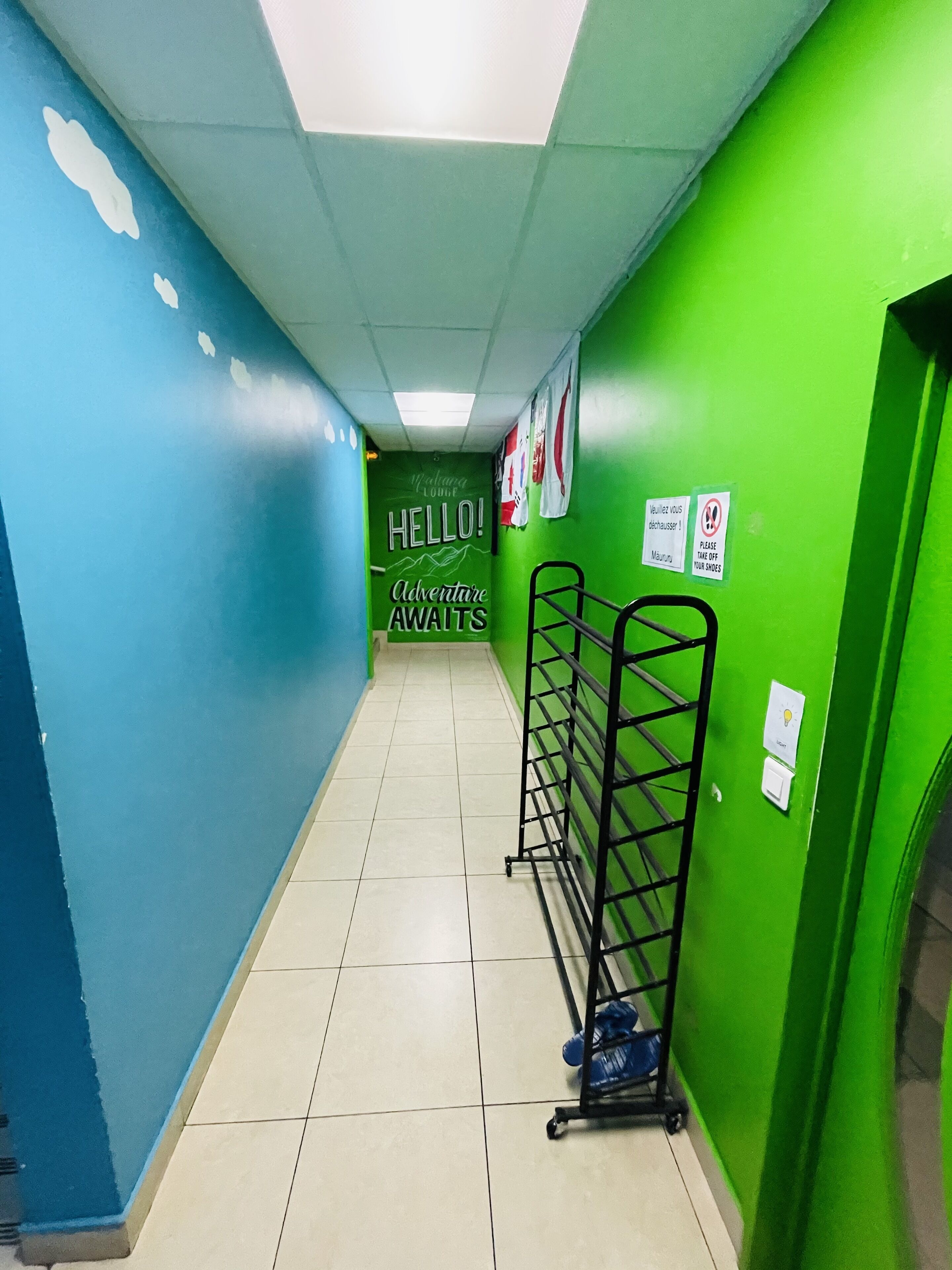 Un pasillo con paredes verdes y azules, un letrero que dice '¡Hola! La aventura te espera' y un perchero con zapatos.