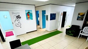 Une pièce spacieuse dotée d’un sol carrelé, d’une moquette verte, d’une table avec des chaises et de divers éléments de décoration murale, notamment des affiches et un motif floral.