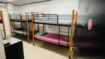 Een studentenkamer met stapelbedden, een zwarte koelkast en een betegelde vloer.