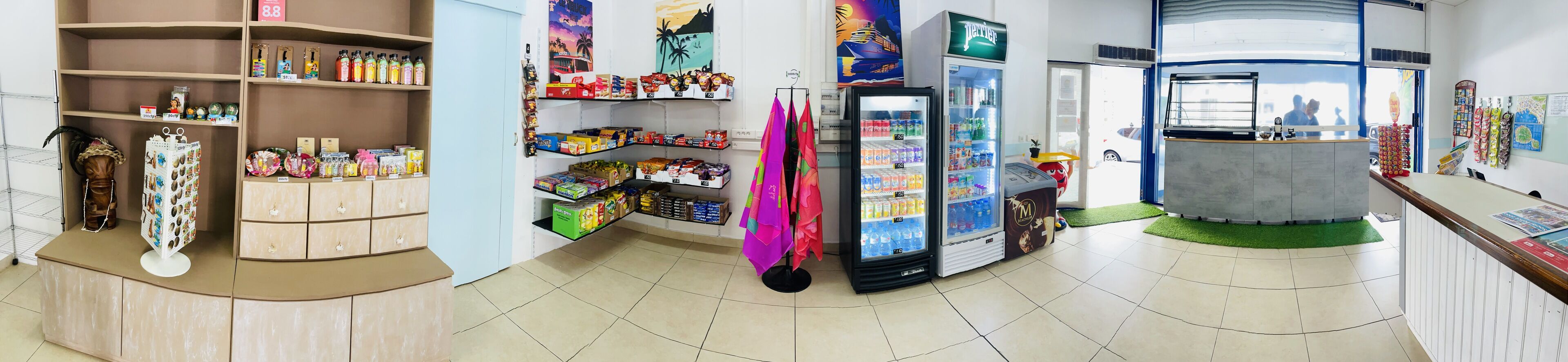 A store with shelves stocked with snacks, a refrigerator with beverages, and a counter with a display.