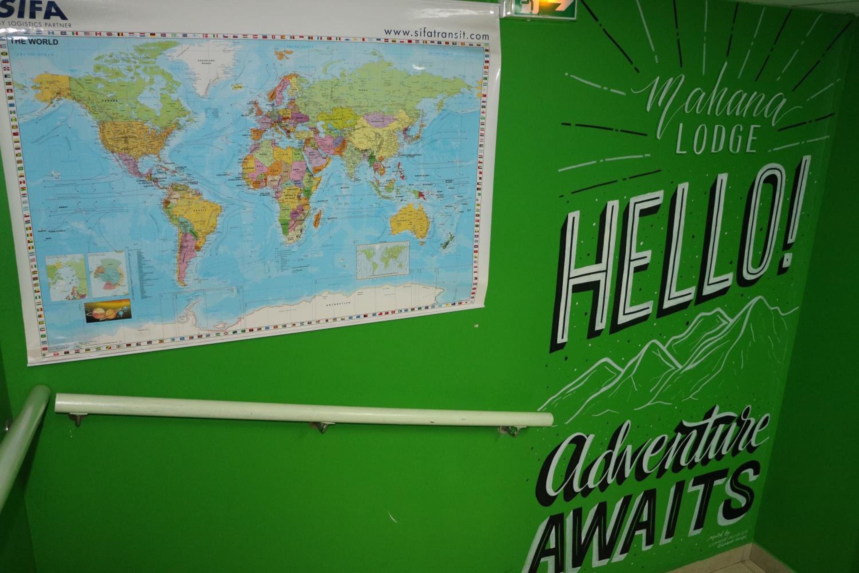 A green wall with a world map and a sign that reads "Mahana Lodge" and "Adventure Awaits".