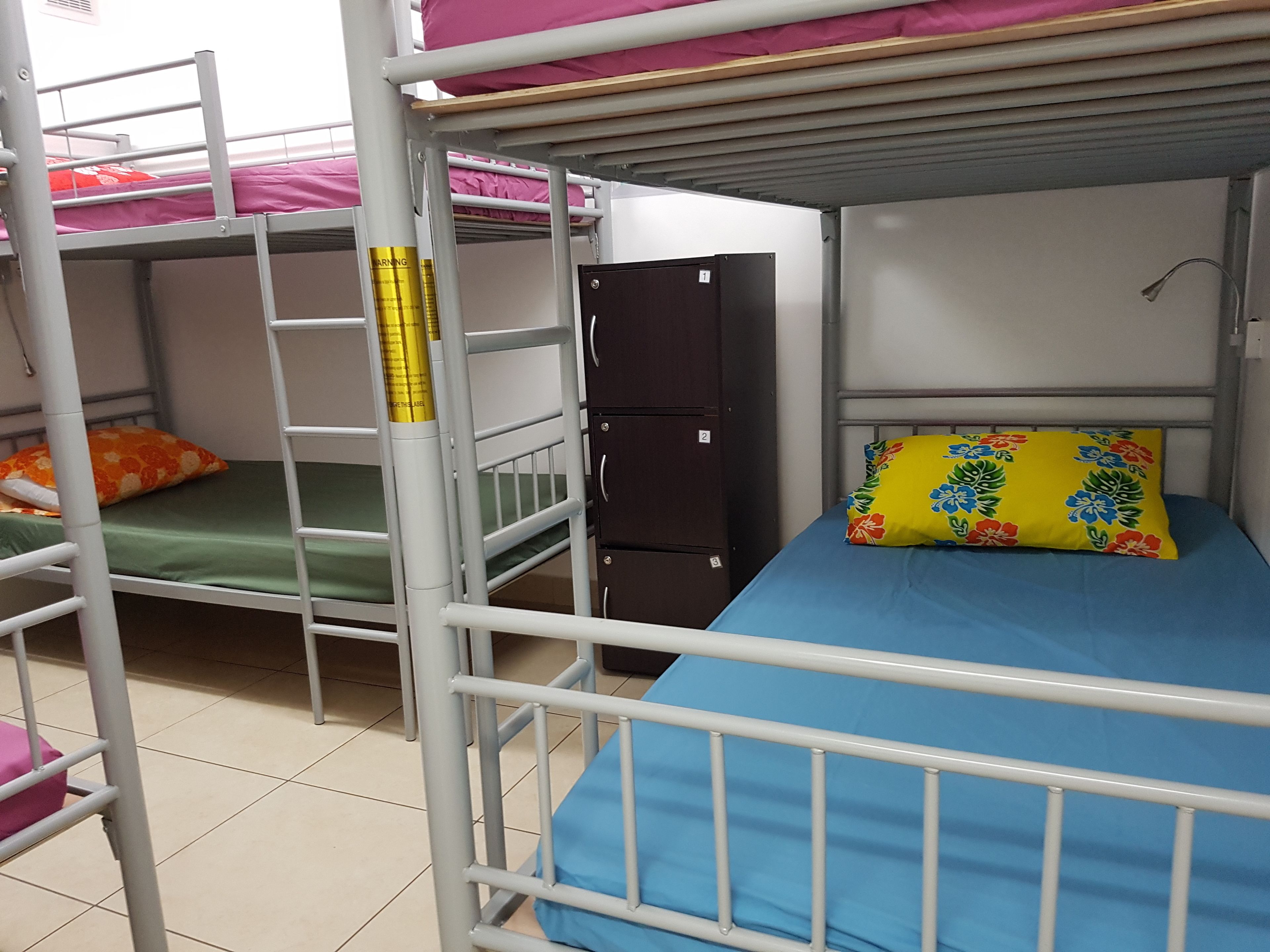 Une chambre avec un lit superposé, une échelle, une armoire et un lit agrémenté d’un coussin à motifs floraux.