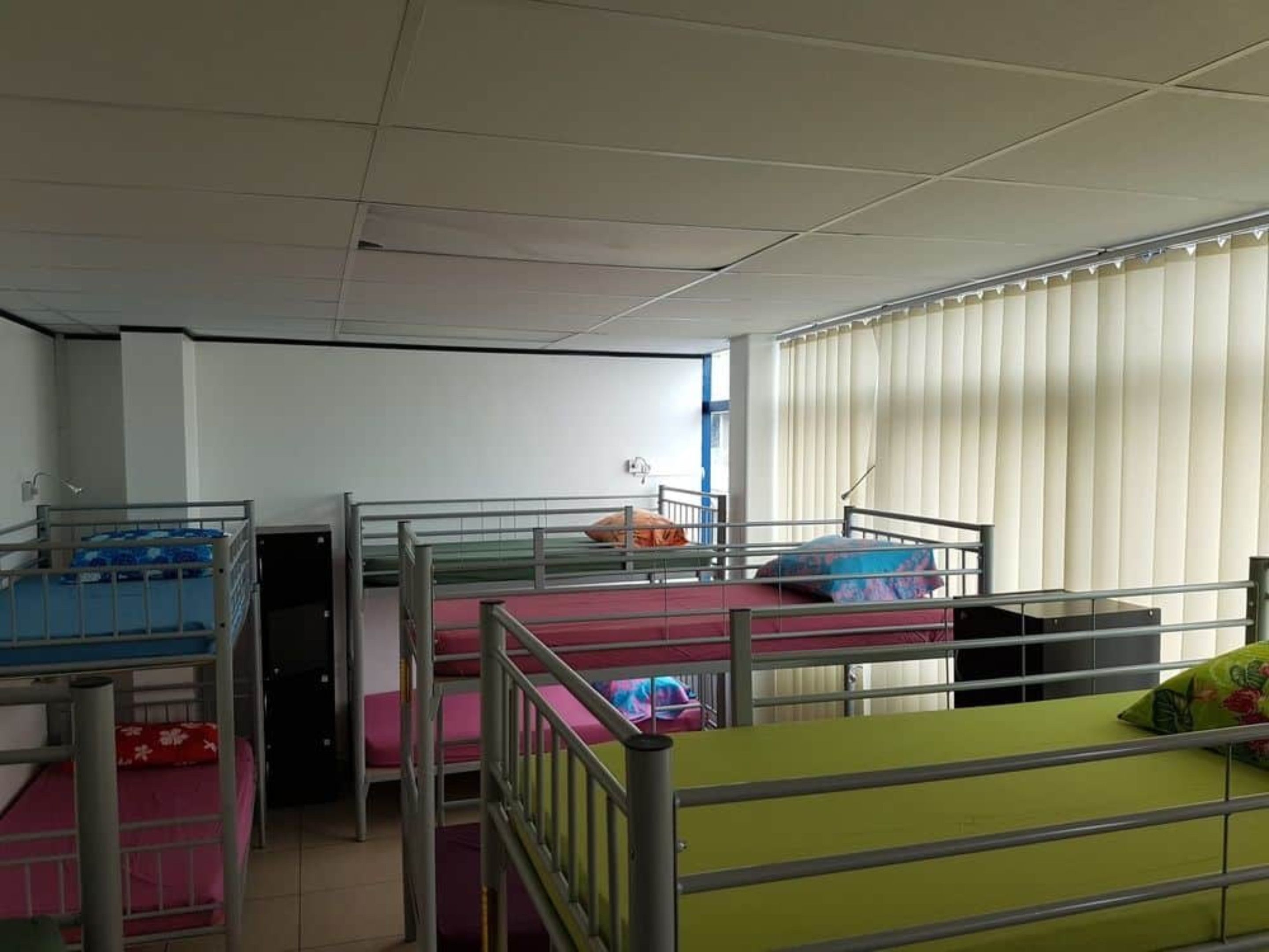 A dormitory room with bunk beds, a window with blinds, and a whiteboard on the wall.