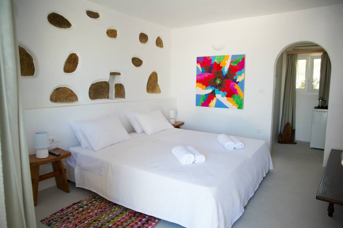 Un dormitorio ordenado con una cama grande, un cuadro abstracto colorido y un diseño de pared de piedra.