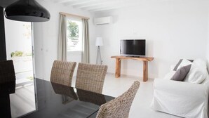 A modern living room with wicker chairs, a glass table, a white sofa, a wooden coffee table, and a TV on a stand. - Bellou Suites (Mykonos)