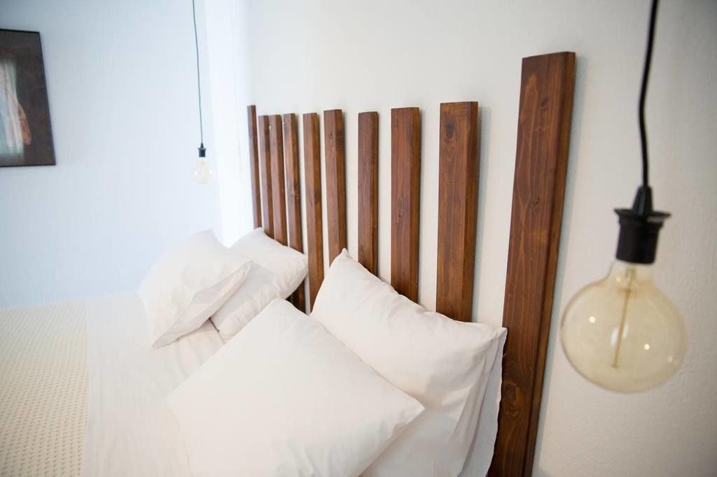 Un lit avec une tête de lit en bois, une literie blanche et une ampoule suspendue.