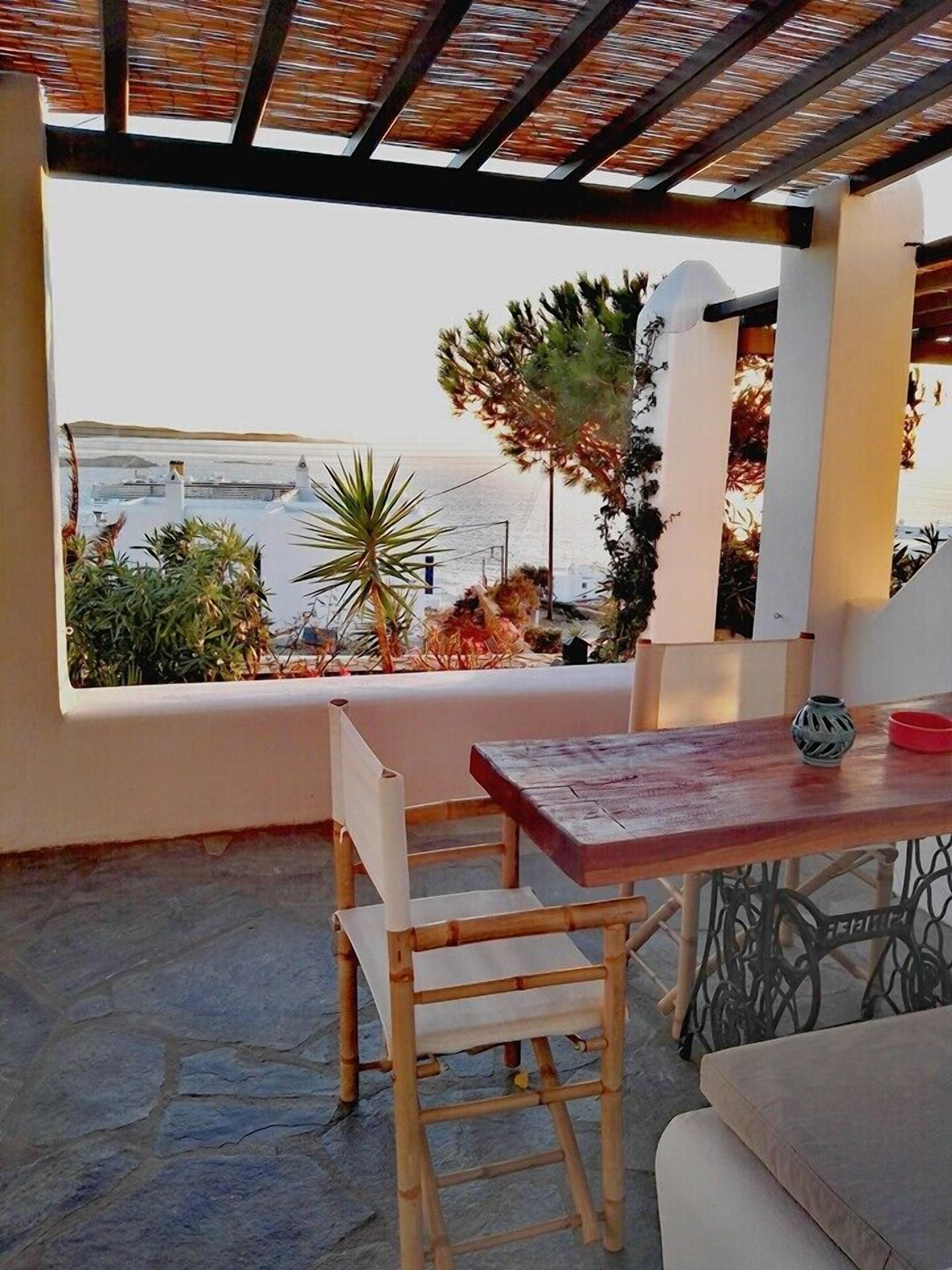 A patio with a table and chairs, a view of the sea, and some plants.