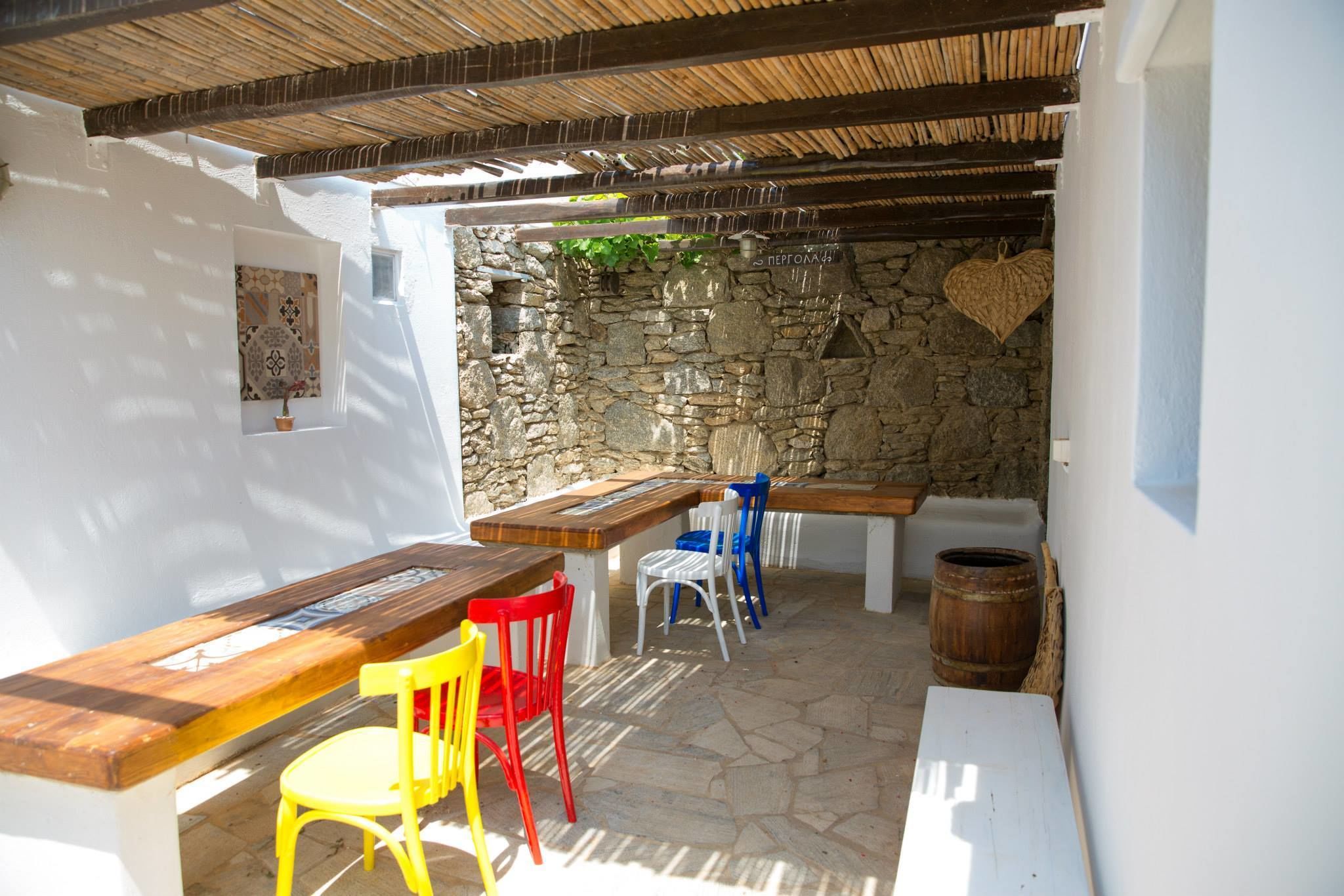 An outdoor patio with a stone wall, wooden furniture, and a thatched roof.