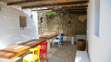 An outdoor patio with a stone wall, wooden furniture, and a thatched roof.