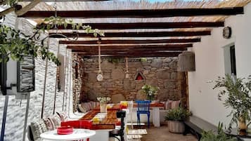 Un espace extérieur aménagé pour les repas, avec un mur en pierre, une pergola en bois et des plantes en pot.