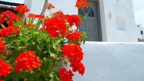 A white building with a bell tower and a door, surrounded by red flowers. - Bellou Suites (Mykonos)