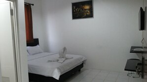 A hotel room with a bed, a painting on the wall, a small table, and a TV mounted on the wall. - De Ritz Hotel (Surabaya)
