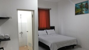 A bedroom with a bed, a shower, a towel, and a painting on the wall. - De Ritz Hotel (Surabaya)