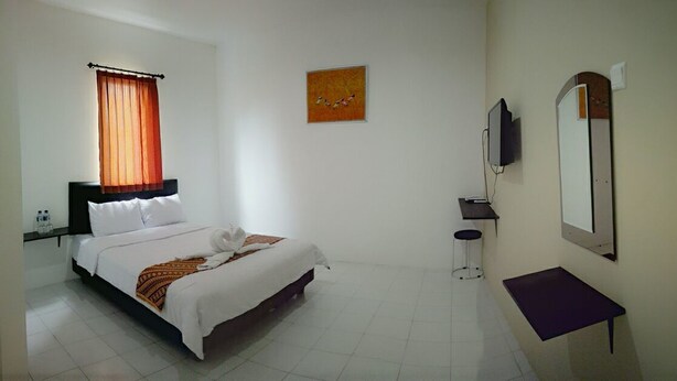 A hotel room with a bed, a TV, a small table, and a painting on the wall. - De Ritz Hotel (Surabaya)