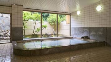 Relax in a serene hot spring bath area with a tranquil garden view through large windows.
