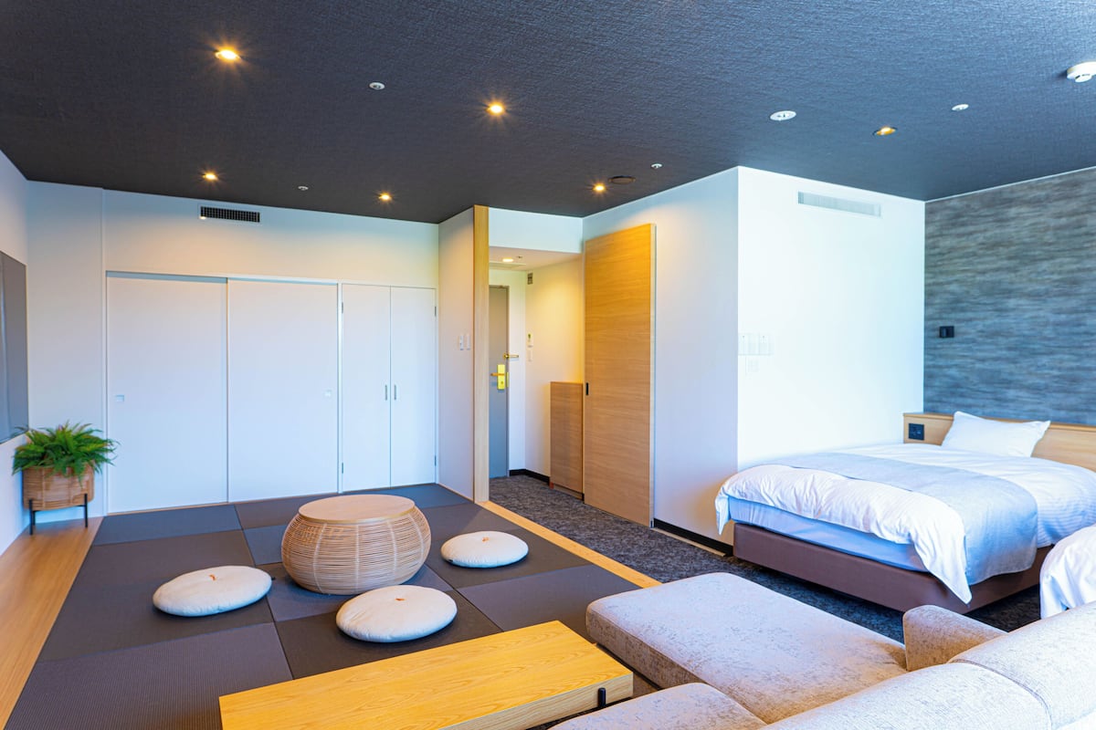 A modern hotel room with a bed, seating area, and a view of the city.