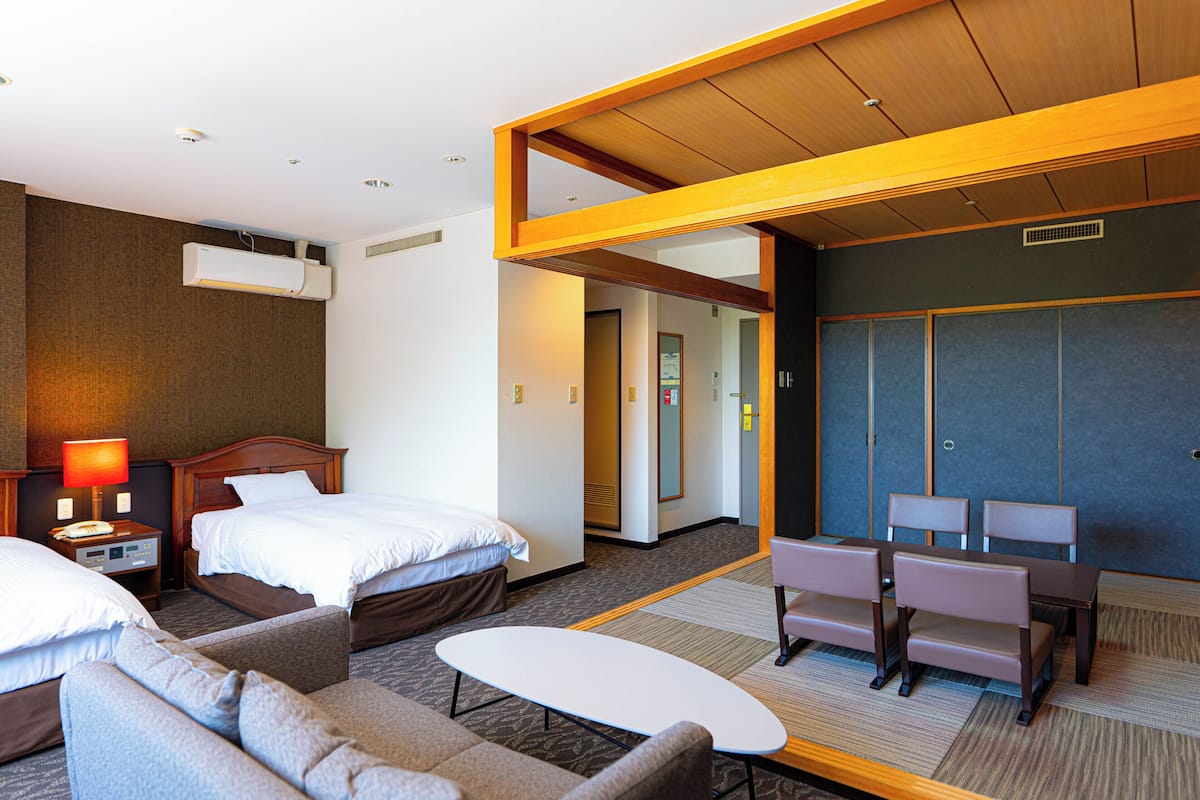 A hotel room with a bed, a sofa, a table, a desk with chairs, and a wardrobe.