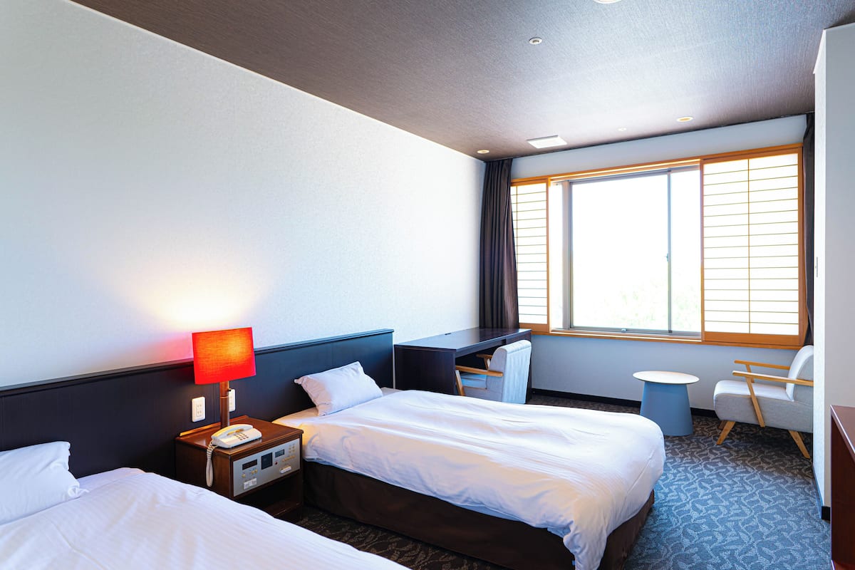 A hotel room with two beds, a desk, a chair, and a small table.