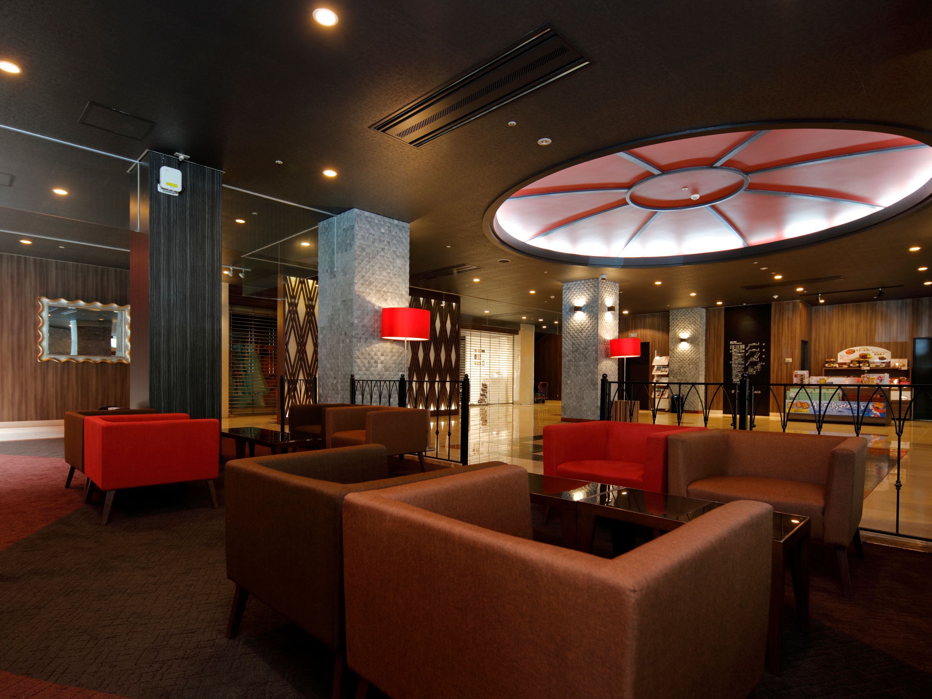 Un lobby moderno con áreas de estar, un elemento central en el techo con iluminación roja, y una barra de restaurante visible.