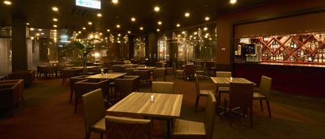 A restaurant with multiple tables and chairs, a bar area with bottles, and a large window in the background.