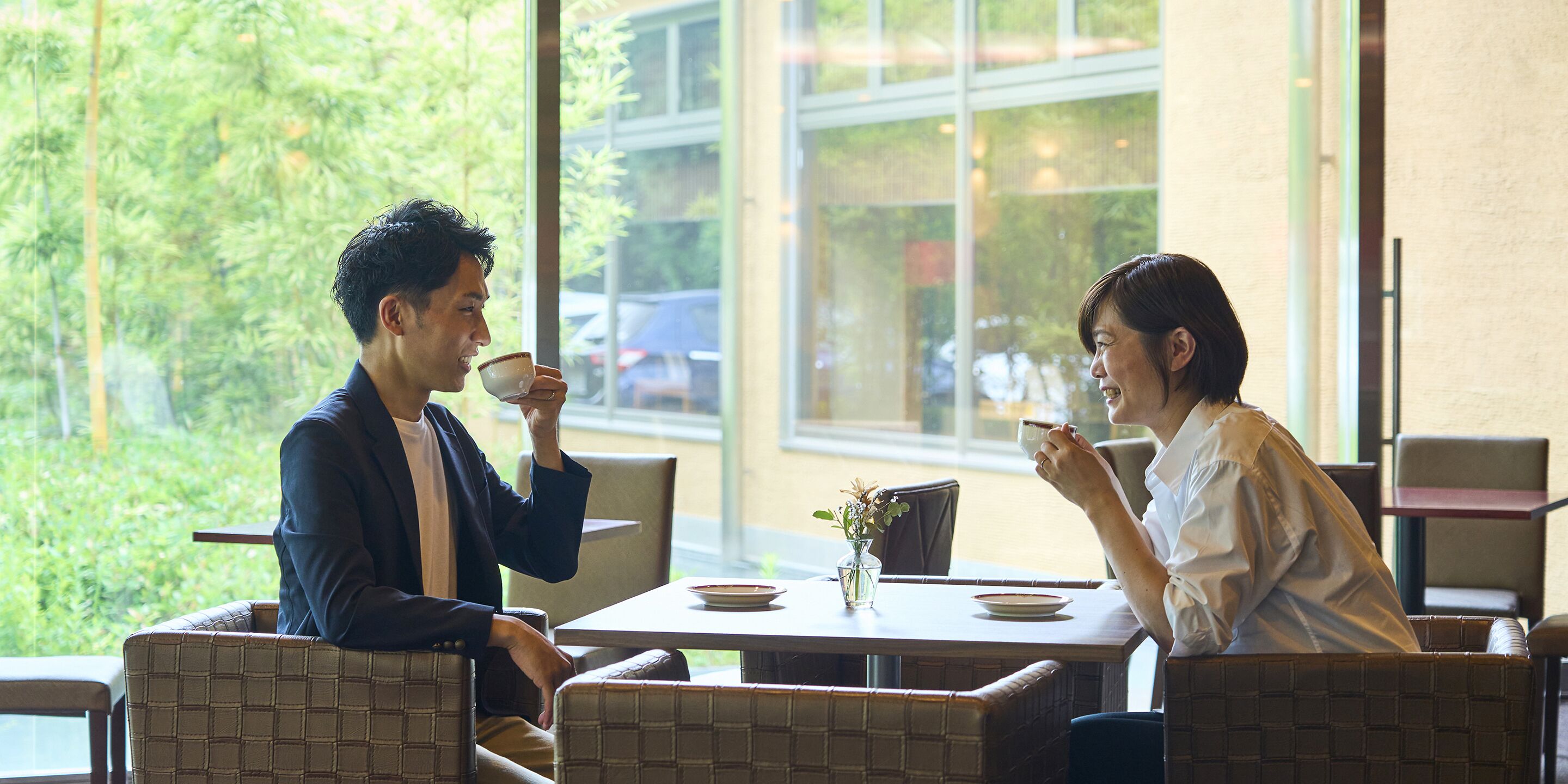 Two people sitting at a table with a view of greenery outside.