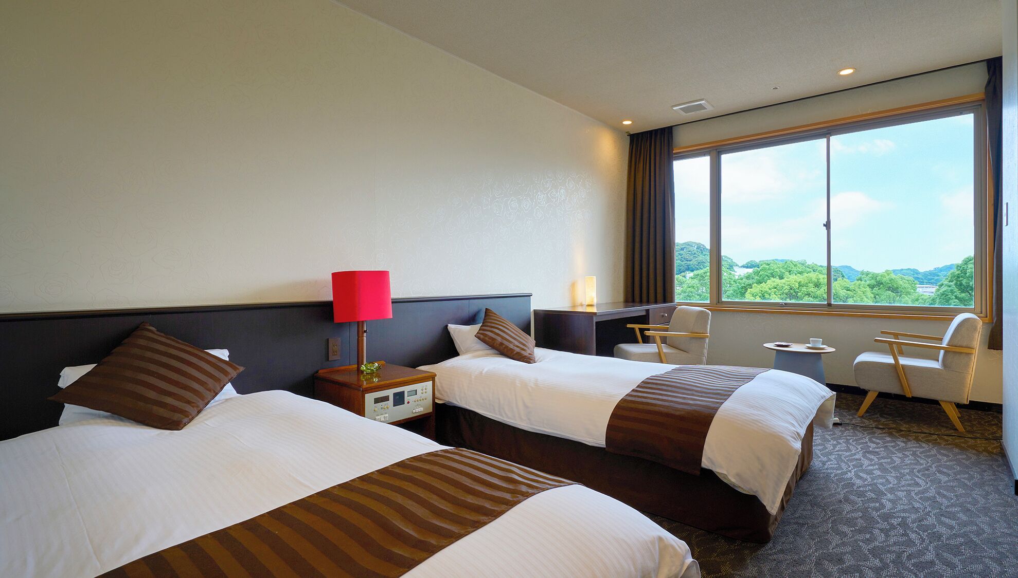 A hotel room with two beds, a desk, a chair, and a large window offering a view.