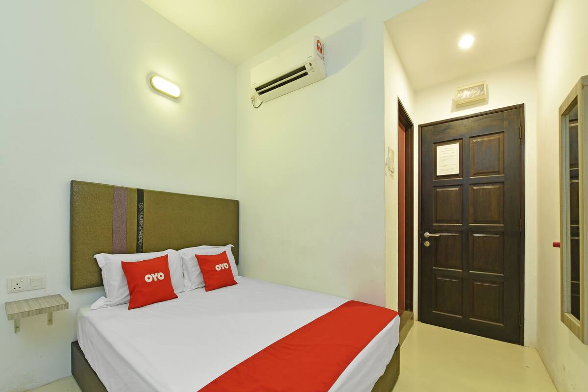 Une chambre d’hôtel comprenant un lit, une table de chevet, un appareil de climatisation, une porte et un interrupteur.