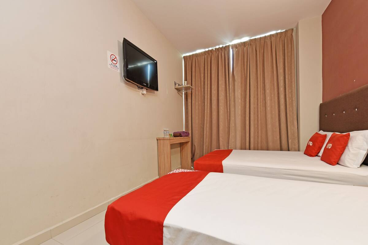 Une chambre d’hôtel avec deux lits, un téléviseur fixé au mur, une petite table avec des articles de toilette et une fenêtre avec des rideaux.