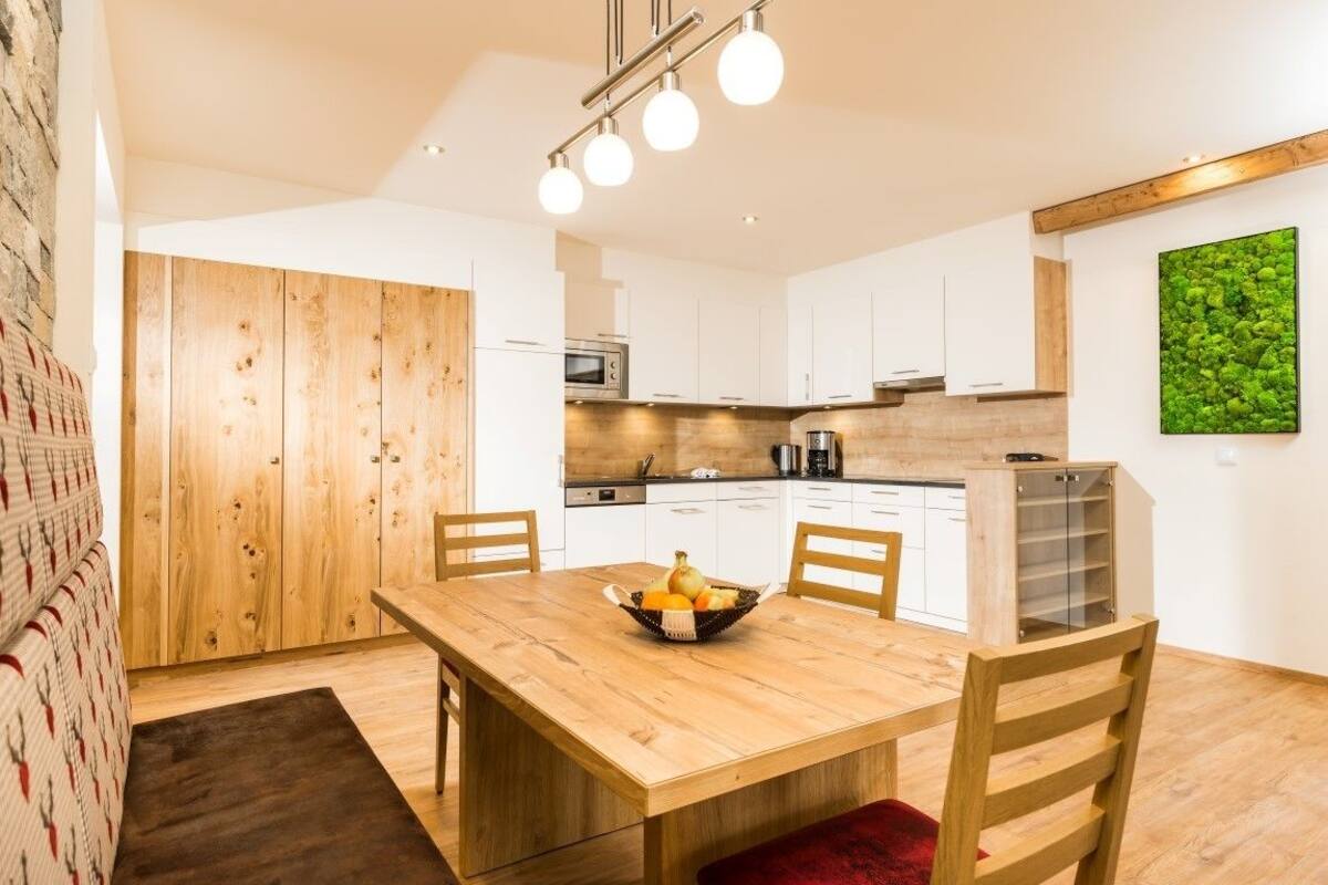 A modern kitchen with white cabinets, a wooden dining table, and a fruit bowl.