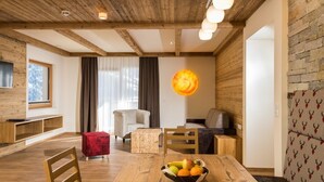 A cozy living room with a wooden ceiling, a dining table with fruit, a red ottoman, and a sofa with a patterned throw. - Luxapart Ambiente (Ladis)