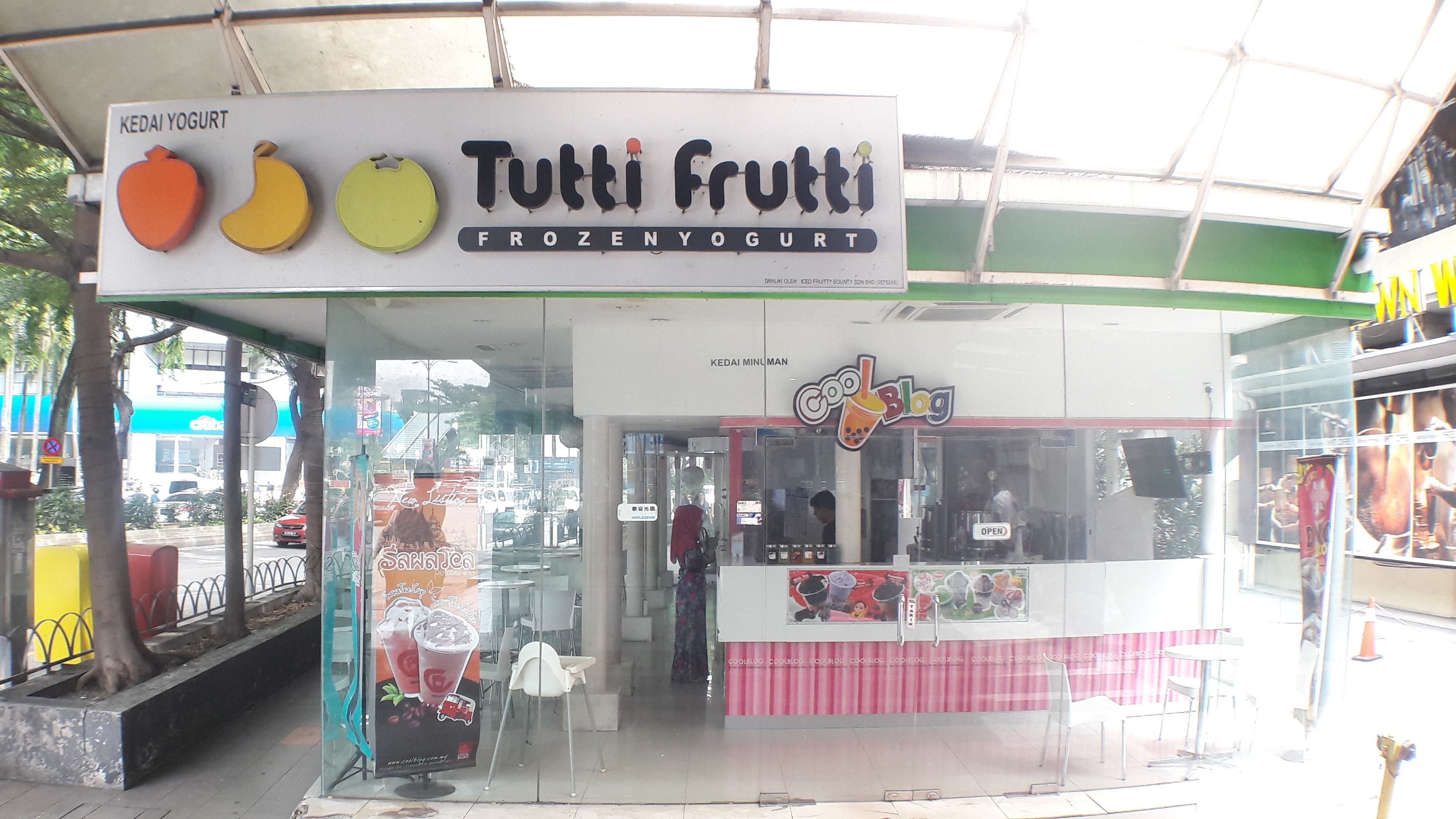 Liikkeen edessä oleva kyltti, jossa lukee: ”Tutti Frutti – pakastettua jogurttia”.