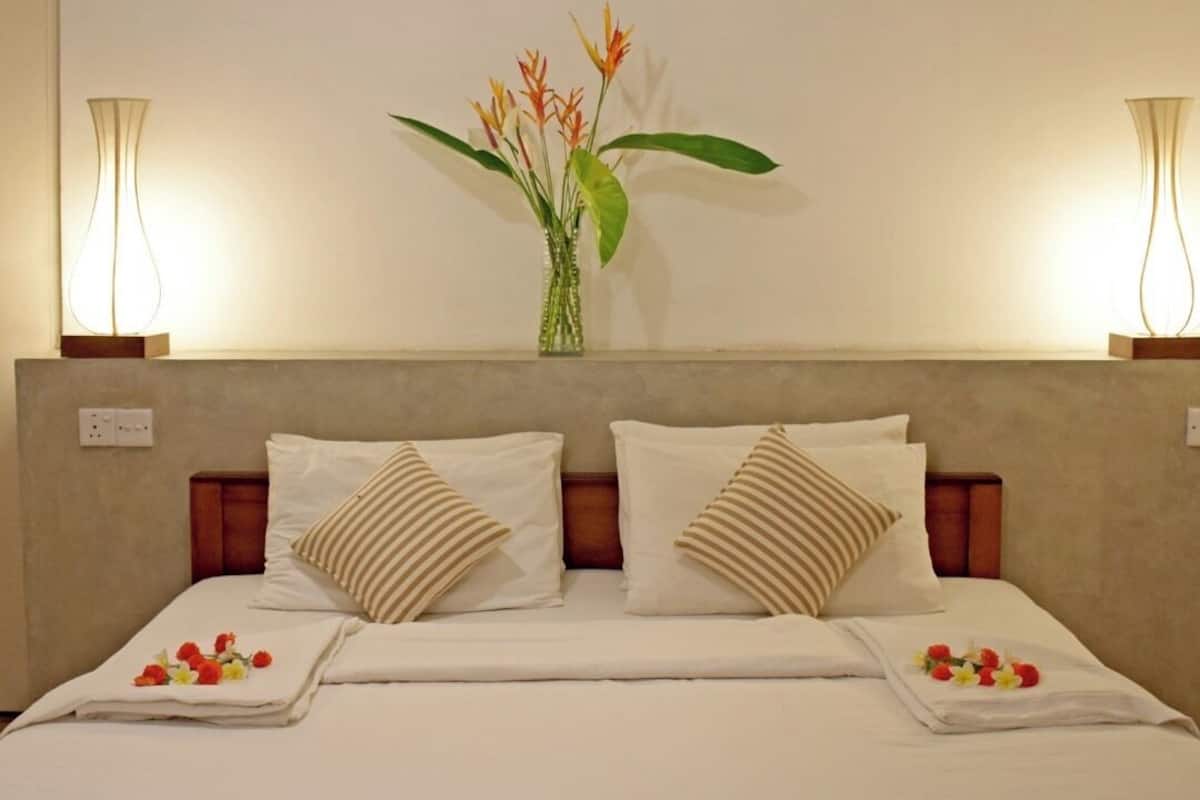 A double bed with two pillows, a vase with flowers, and two wall-mounted lamps.
