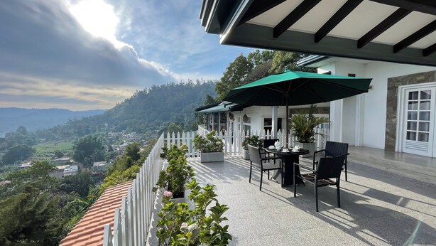 A terrace with outdoor seating, a white picket fence, and a view of a mountainous landscape. - Villa Perpetua (Bandarawela)