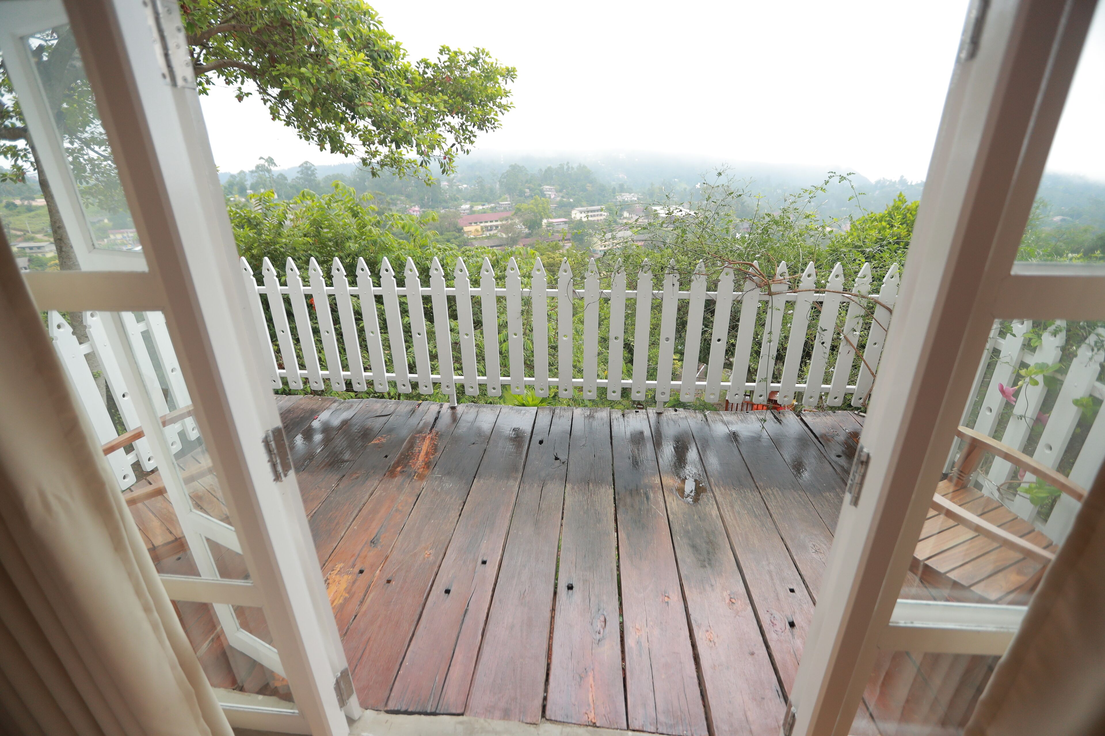 Een houten terras met een witte picket fence, dat uitkomt op een uitzicht over een woonwijk.