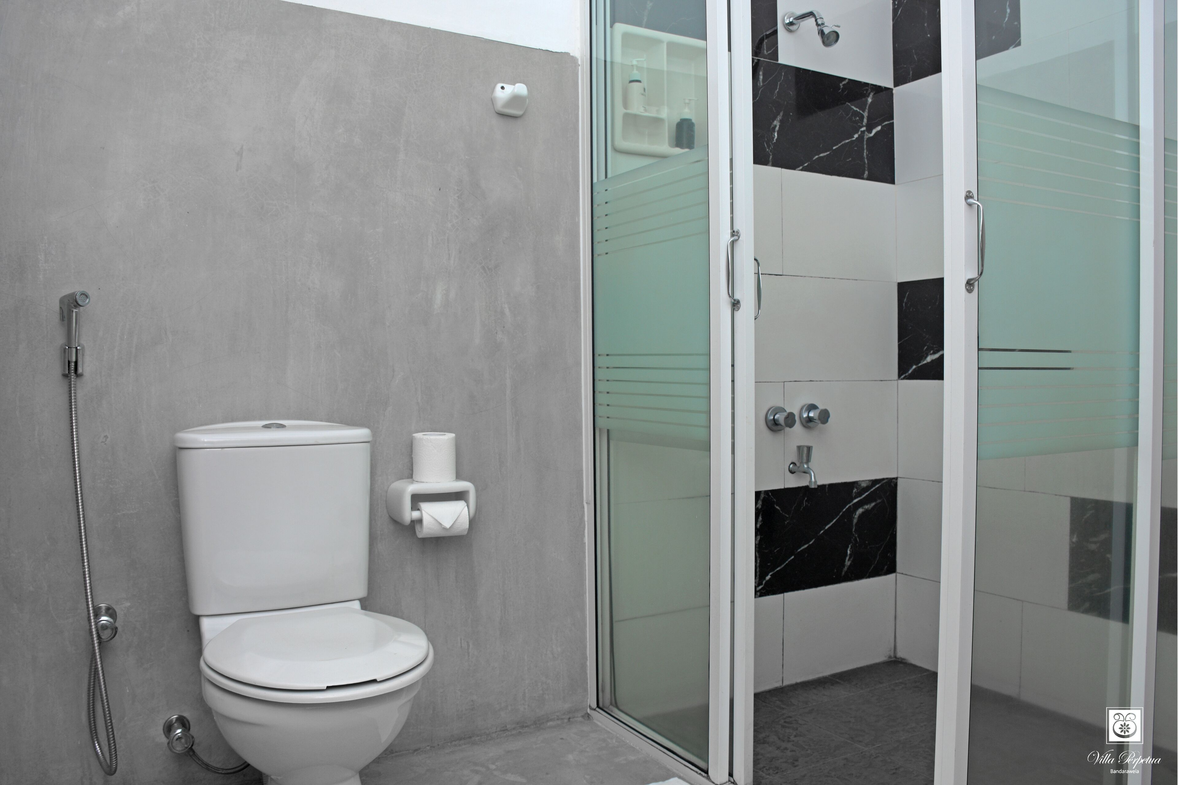 Une salle de bain moderne équipée de toilettes, d’une douche et d’un espace douche fermé par des parois de verre.