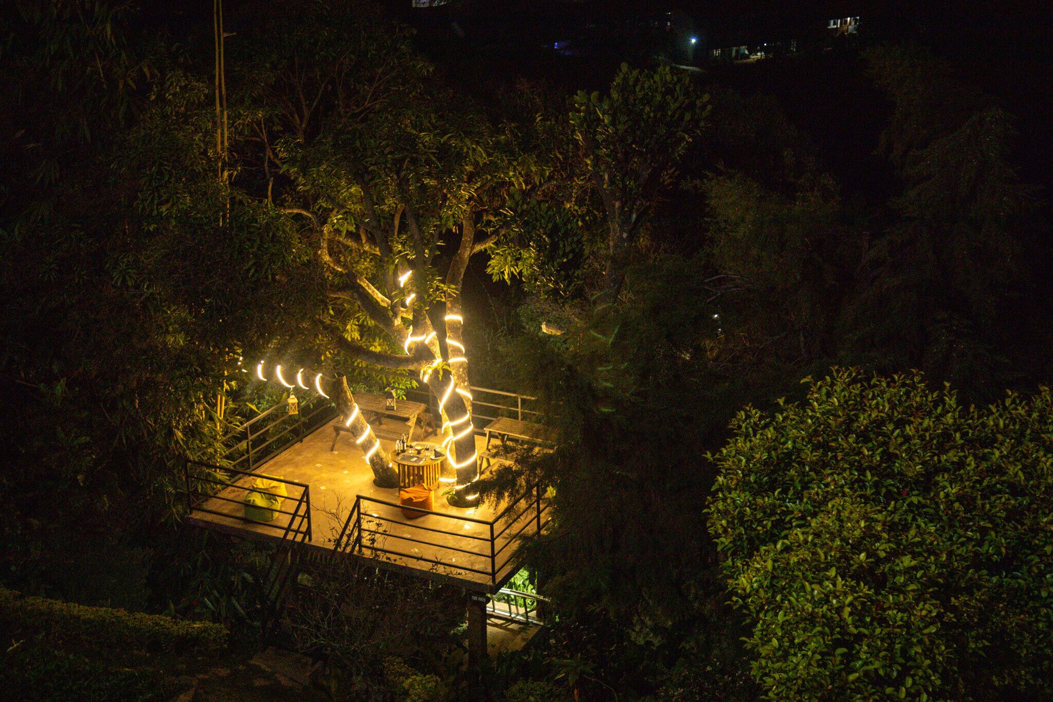 A nighttime view of a garden with a central light installation and a small platform with seating.