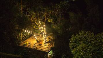 A nighttime view of a garden with a central light installation and a small platform with seating.