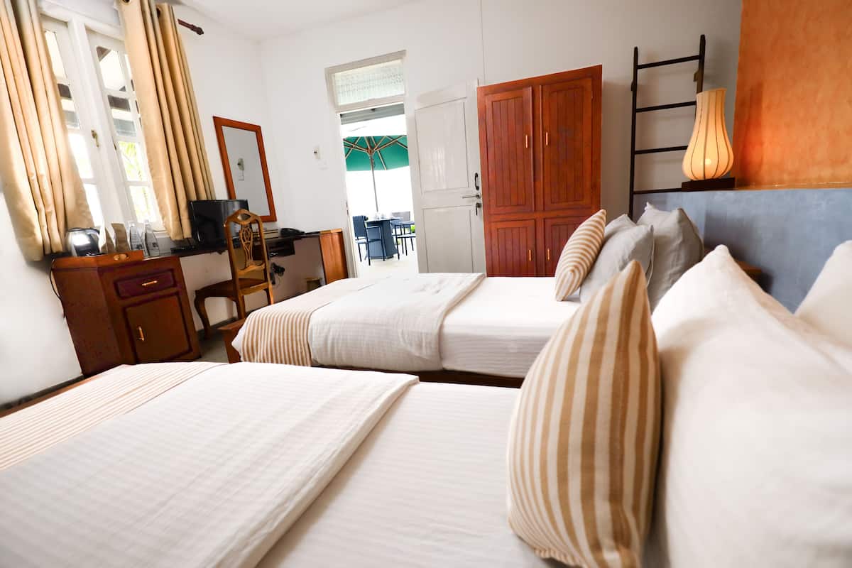 A hotel room with two beds, a desk, a chair, a wardrobe, and a view of the outside.