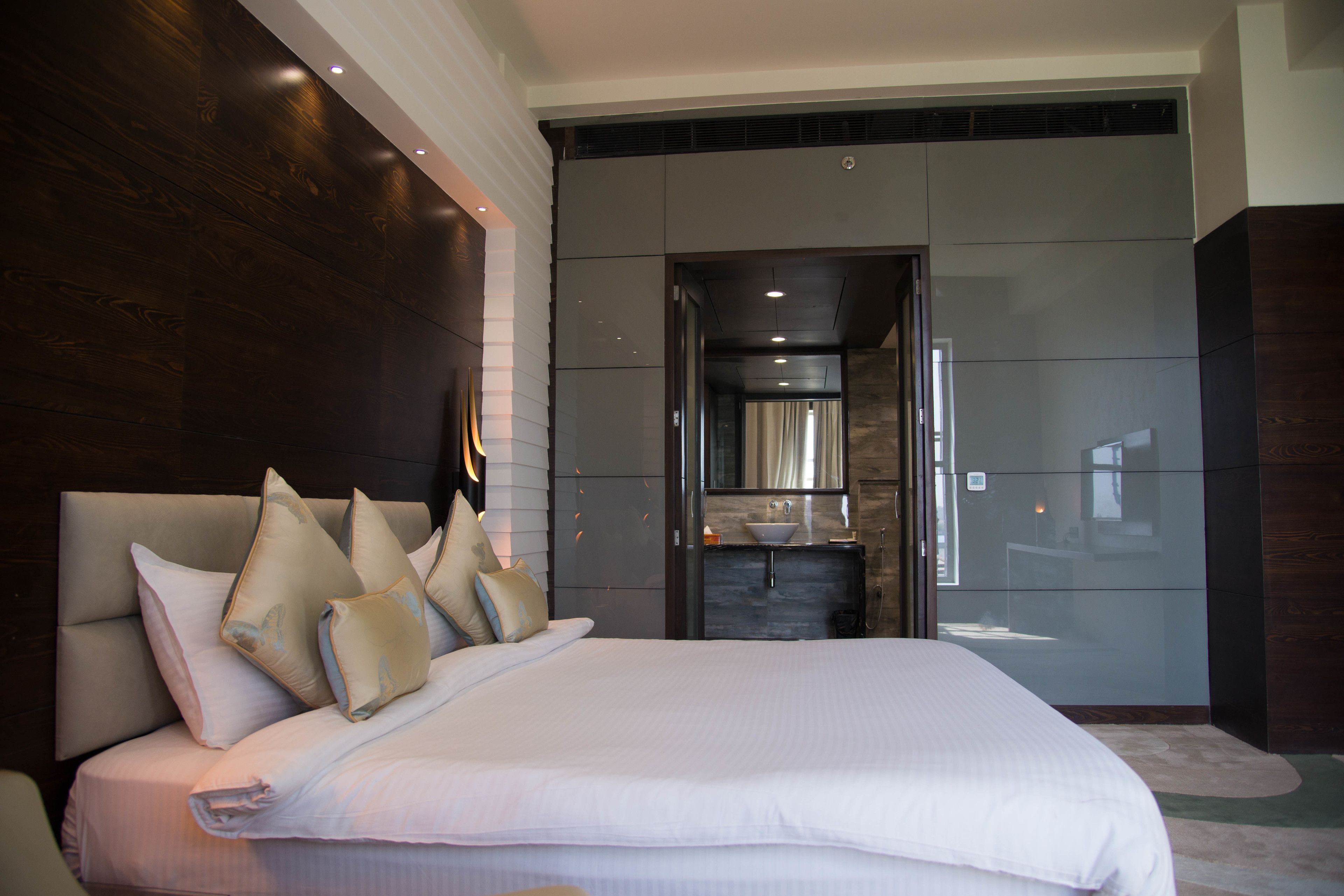 A modern hotel room with a large bed, a built-in vanity, and a view of the city.