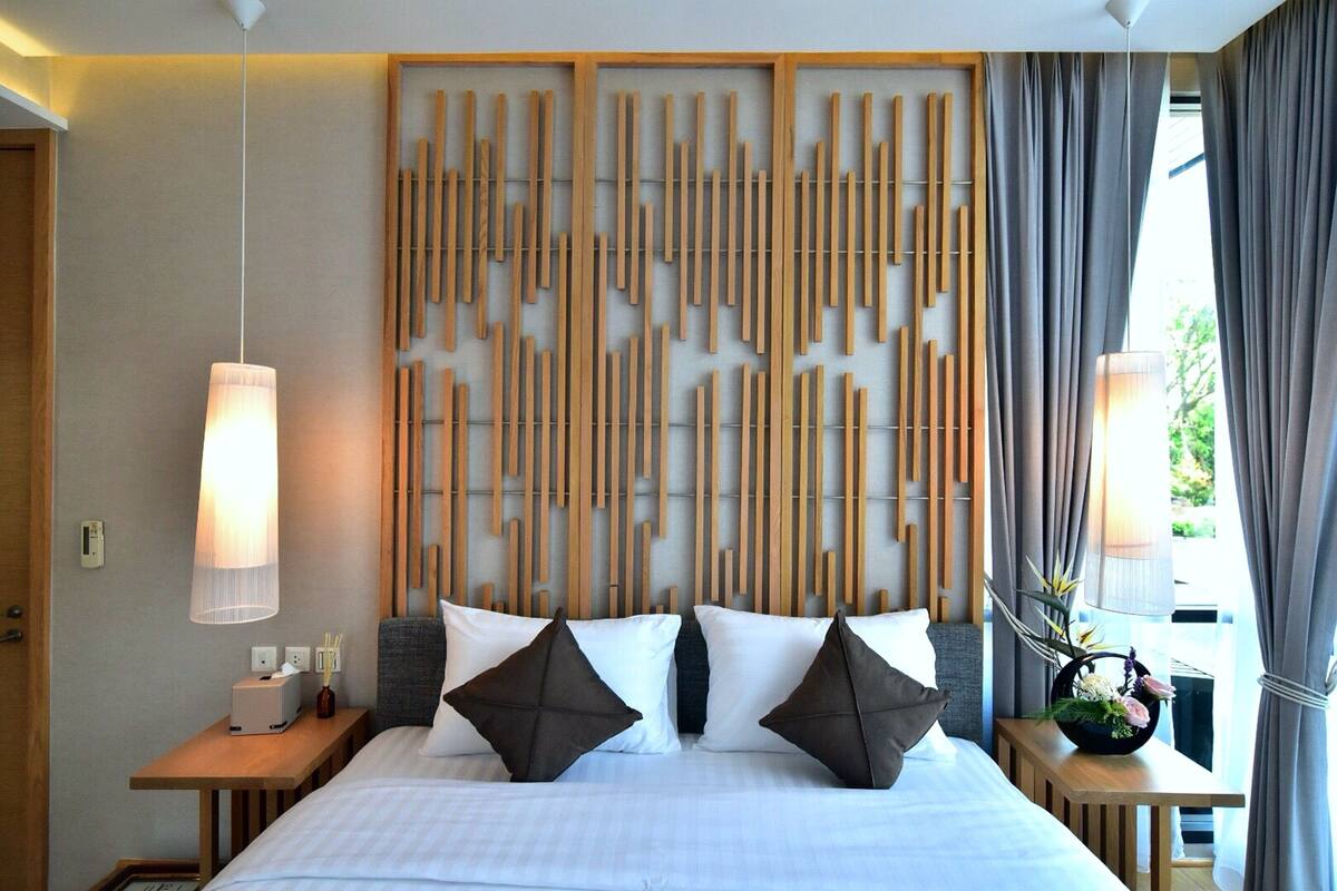 A hotel room with a bed, bedside tables, a wall-mounted light fixture, and a window with curtains.
