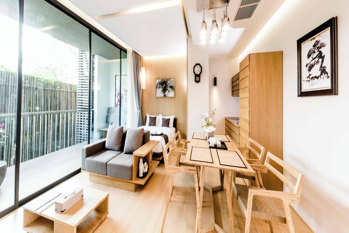 A modern living room with a sofa, a dining table with chairs, a large window, and a clock on the wall.