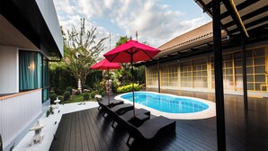 A modern outdoor pool area with a wooden deck, lounge chairs, and a red umbrella. - Zen Villa Khao Yai (Pak Chong)