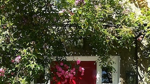 A red door with a white frame, surrounded by lush greenery and pink flowers. - Ballylagan Organic Farm (Ballyclare)