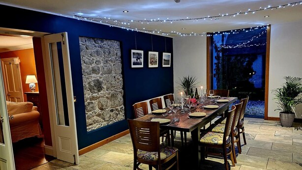 A dining area with a stone wall, a long wooden table set for six, and a view of the outdoors. - Ballylagan Organic Farm (Ballyclare)