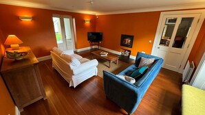 A living room with a white sofa, a blue armchair, a wooden coffee table, and a television. - Ballylagan Organic Farm (Ballyclare)