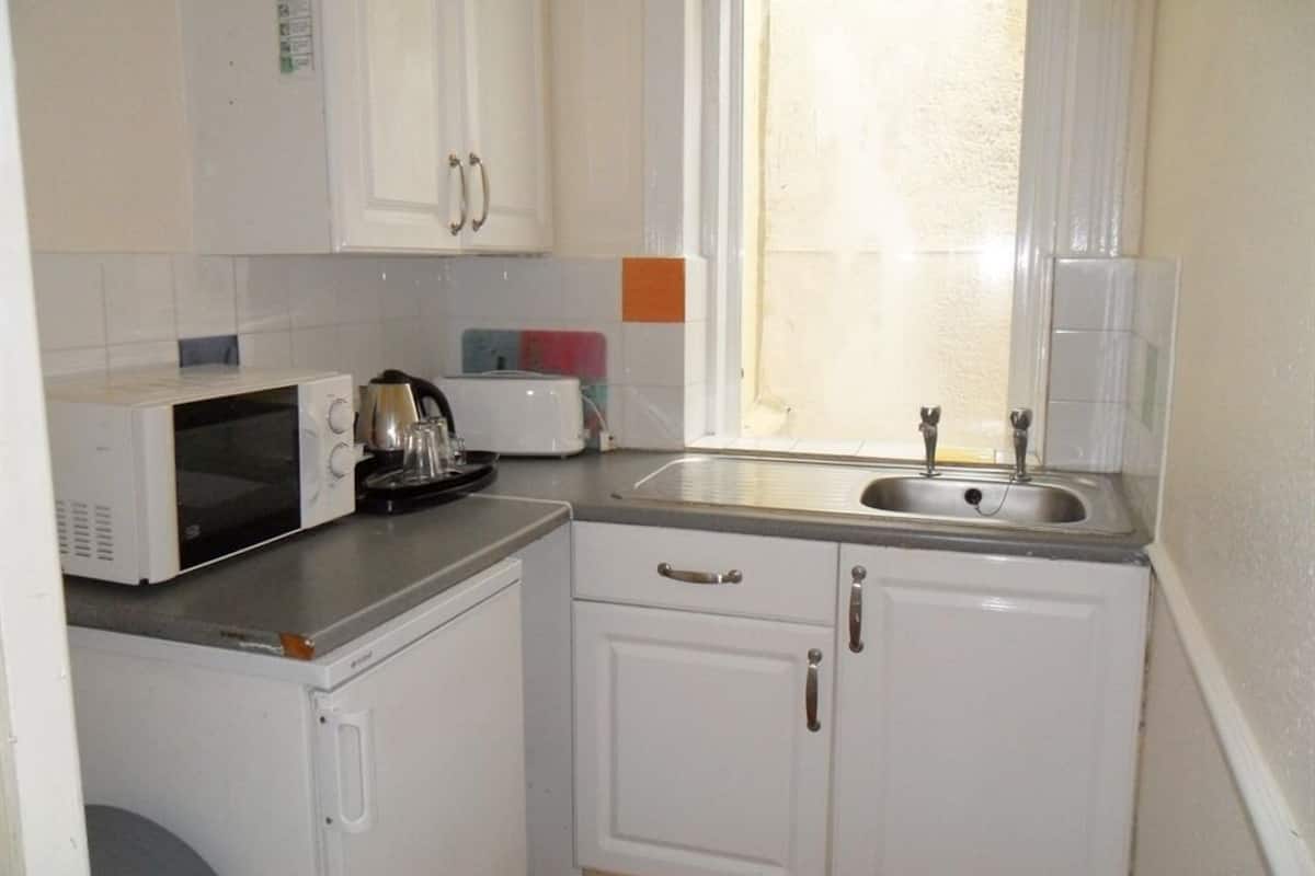 A compact kitchen with white cabinets, a microwave, a kettle, and a sink.