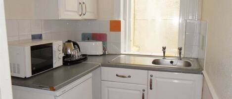 A compact kitchen with white cabinets, a microwave, a kettle, and a sink.