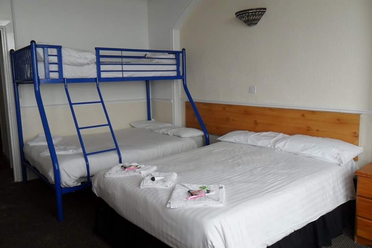 A room with bunk beds, a wooden headboard, a bedside table, and a wall-mounted light fixture.